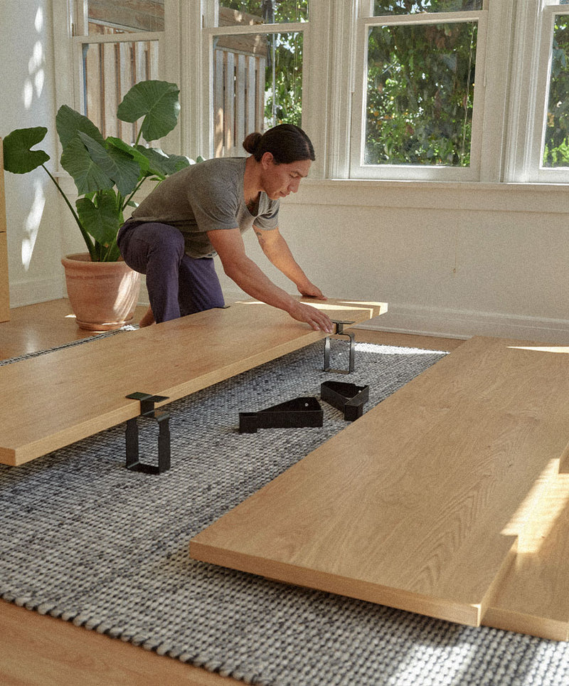 Adapt and evolve your Bed Frame. A man, kneeling on the floor, adjusts the base of his Floyd Bed.